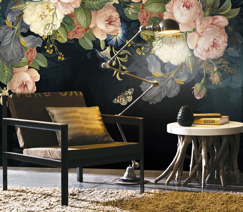 May include: A black armchair with a brown cushion and a throw pillow sits in front of a dark floral wallpaper with a butterfly and a lamp. A small wooden table with a white top and a black decorative object sits next to the chair. The table has a book titled "Jazzlife" on top.