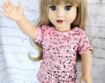 May include: A pink sequined dress with short sleeves and a round neckline. The dress is worn by a doll with blonde hair and blue eyes.