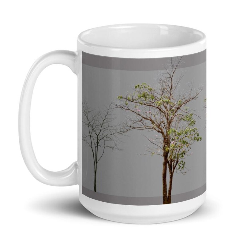 May include: White ceramic mug with a design of three trees with different stages of leaf growth. The trees are on a gray background.