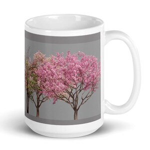 May include: White ceramic mug with a gray background and a design of three pink flowering trees. The trees are in a row and have green leaves.