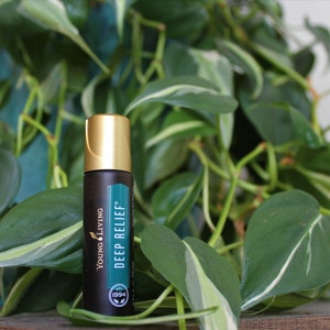 Op de afbeelding: Een donkerbruine rollerfles met essentiële olie en een gouden dop, met het label "Deep Relief" van Young Living. De fles staat tegen een achtergrond van weelderige groene bladeren, wat een natuurlijke uitstraling creëert. Het productlabel bevat het jaar 1994.