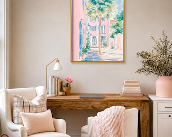 May include: A framed wall art print featuring a watercolor-style painting of a pink building with blue shutters and a tall palm tree in a sunny courtyard. The artwork is displayed in a thin gold frame and depicts a bright, outdoor scene.