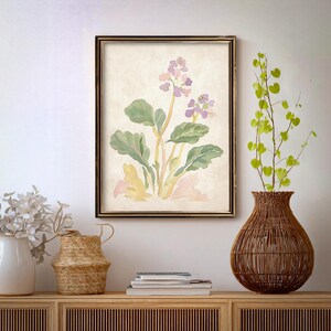 May include: A framed watercolor painting of a botanical illustration featuring purple flowers, green leaves, and yellow stems. The artwork is displayed on a light-colored wall above a wooden cabinet with decorative vases and a woven vase.