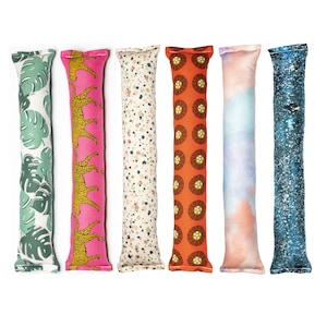 May include: Six colorful catnip toys in the shape of long pillows. The toys have different patterns, including a pink leopard print, a green tropical leaf print, a beige speckled print, an orange floral print, a blue watercolor print, and a blue glitter print.