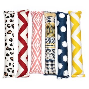May include: Six catnip toys with different patterns. The toys are made of fabric and are filled with catnip. The patterns include leopard print, red and white zigzags, pink and white diamonds, blue and yellow tribal print, blue and white polka dots, and yellow and white zigzags.