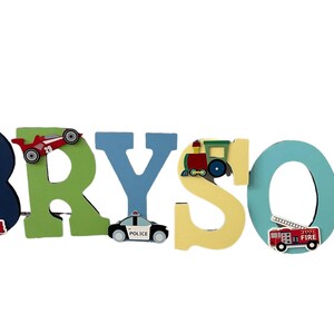 Puede incluir: Letrero de nombre de madera que deletrea "BRYSON" en varios colores. Cada letra est&aacute; decorada con un veh&iacute;culo diferente, incluyendo un coche de carreras rojo, un coche de polic&iacute;a, un tren, un cami&oacute;n de bomberos y un cami&oacute;n rojo. Una pieza decorativa para la habitaci&oacute;n de un ni&ntilde;o.