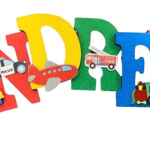 Puede incluir: Letras de madera de colores que deletrean un nombre, decoradas con veh&iacute;culos de juguete. Las letras son rojas, amarillas, verdes y azules. Coches de juguete, un coche de polic&iacute;a, un avi&oacute;n, un cami&oacute;n de bomberos y un tren est&aacute;n adjuntos.