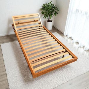 May include: A light brown wooden bed frame featuring a slatted base and an adjustable headrest section. The rectangular frame is constructed from natural wood with visible grain, providing a sturdy foundation for a mattress in a bedroom setting.