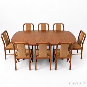 May include: A large oval wooden dining table with a smooth grain finish, accompanied by eight matching chairs. Each chair features a curved wooden frame and a rectangular backrest upholstered in a textured, light brown fabric material.