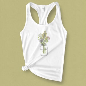 May include: White tank top with a floral design in a mason jar. The flowers are pink, yellow, and white.