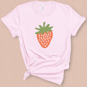 May include: A pink t-shirt with a stylized illustration of a red strawberry with green leaves.