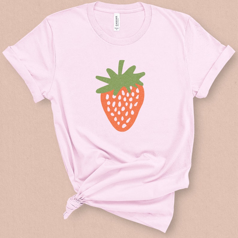 May include: A pink t-shirt with a stylized illustration of a red strawberry with green leaves.