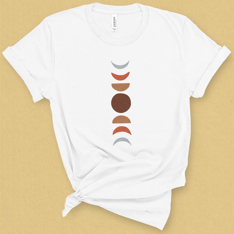 May include: White t-shirt with a vertical design of a moon phases graphic in shades of gray, brown, and orange.