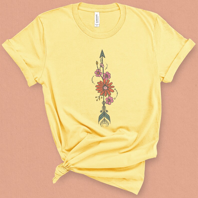 May include: A yellow t-shirt with a floral arrow design. The arrow is green and brown with pink and red flowers.