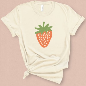 May include: A cream colored t-shirt with a stylized red strawberry with green leaves printed on the front.