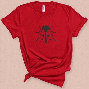 Puede incluir: Camiseta roja con un gr&aacute;fico de mariquita negra.