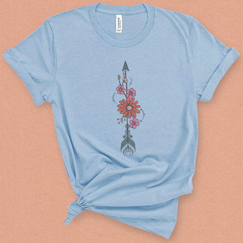 May include: A light blue t-shirt with a floral arrow design. The arrow is decorated with pink and orange flowers and green leaves.