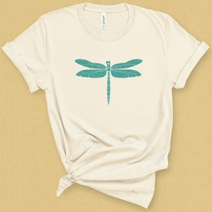 May include: A cream colored t-shirt with a teal dragonfly graphic.