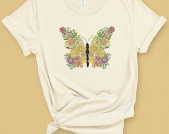 Peut inclure: Un t-shirt blanc avec un motif de papillon floral. Le papillon est composé de fleurs jaunes, roses et vertes.