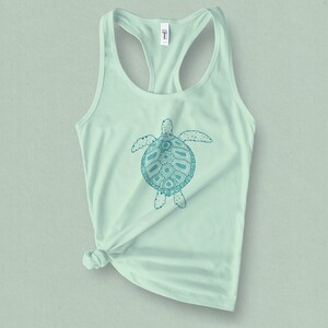 May include: A light green tank top with a teal blue graphic of a stylized sea turtle. The turtle has a detailed design with intricate patterns.