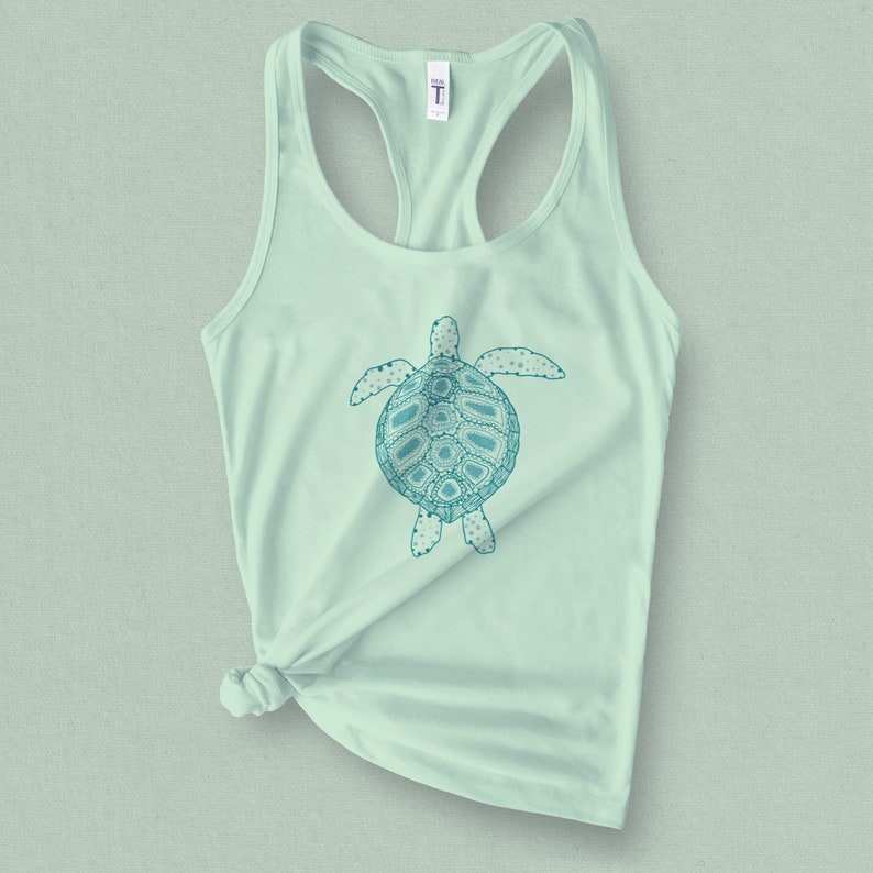 May include: A light green tank top with a teal blue graphic of a stylized sea turtle. The turtle has a detailed design with intricate patterns.