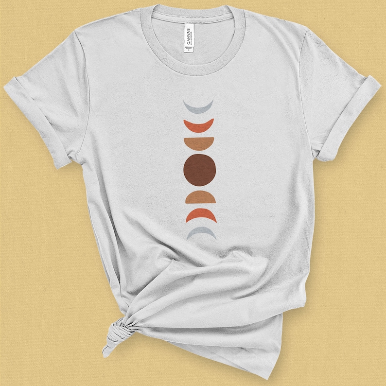 May include: White t-shirt with a graphic of a vertical line of abstract moons in shades of gray, red, orange, and brown.