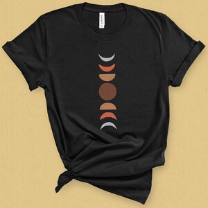 May include: Black t-shirt with a graphic of a moon phases design in shades of gray, red, orange, and brown.