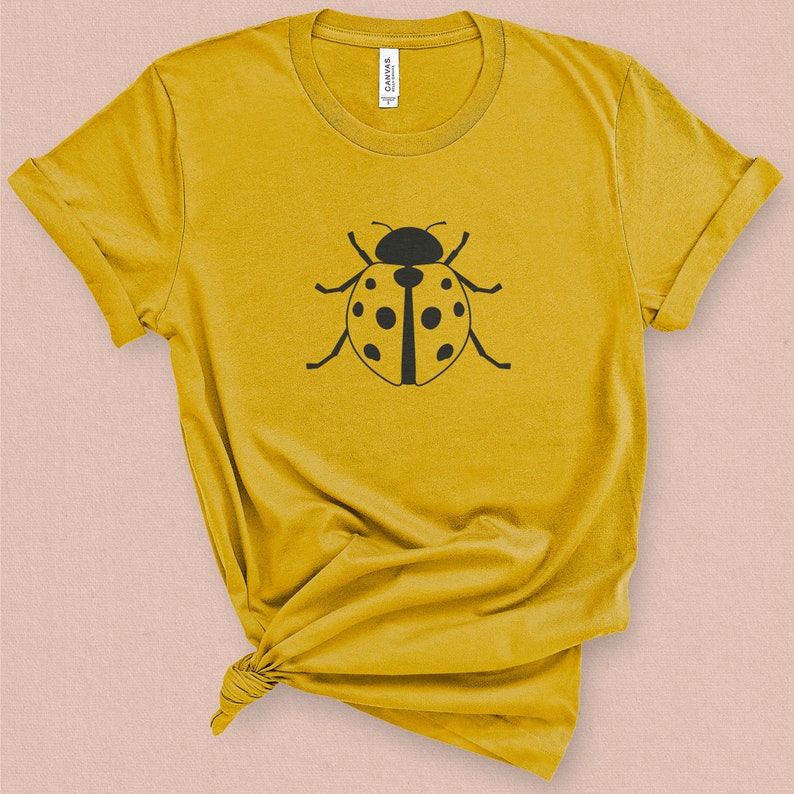 Puede incluir: Una camiseta amarilla con un gr&aacute;fico de mariquita negra en la parte delantera.