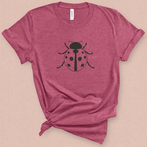 Puede incluir: Una camiseta color granate con un gr&aacute;fico de mariquita negra en la parte delantera.