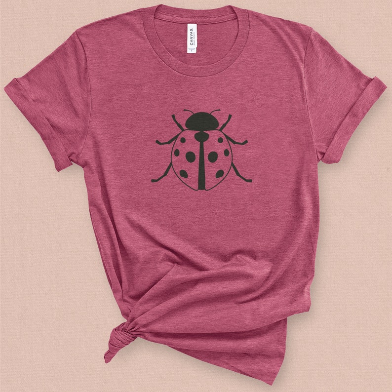 Puede incluir: Una camiseta color granate con un gr&aacute;fico de mariquita negra en la parte delantera.