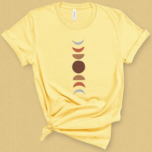 May include: A yellow t-shirt with a graphic of a stylized moon phases design in brown, red, and blue colors.