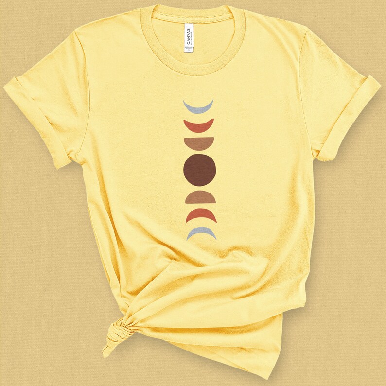 May include: A yellow t-shirt with a graphic of a stylized moon phases design in brown, red, and blue colors.