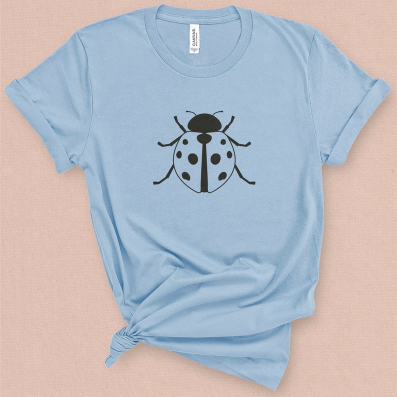 Puede incluir: Una camiseta azul claro con un gr&aacute;fico de mariquita negra.