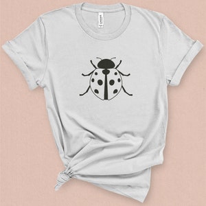 Puede incluir: Una camiseta blanca con un gr&aacute;fico de mariquita negra impreso en la parte delantera.