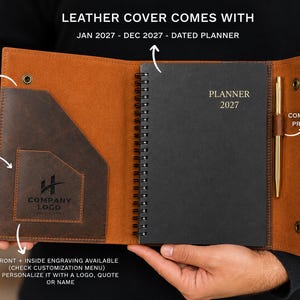 May include: A brown leather planner cover featuring a document sleeve, a business card holder with a company logo, and a spiral-bound black planner dated Jan 2027 - Dec 2027. A gold-colored pen is held in a side loop, and the cover has snap closures.