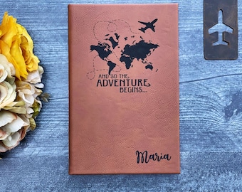 May include: Brown leather journal with a world map and airplane design. The text "And so the adventure begins..." is printed on the cover. The name "Maria" is personalized on the bottom of the journal.
