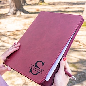 May include: A burgundy leather zippered binder with a black monogrammed initial "S" and the name "Sophia" printed on the front.