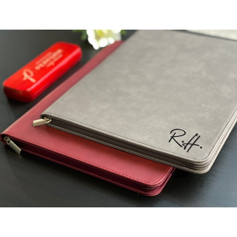 May include: Two zippered leather folders, one gray and one burgundy. The gray folder has the initials "R.H." embossed on the front.