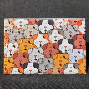 May include: A white rectangular magnet with a pattern of colorful guinea pigs. The guinea pigs are all facing forward and have different colored fur, including brown, white, orange, and black.