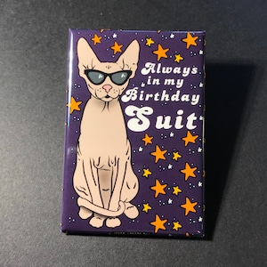 Puede incluir: Un fondo morado con estrellas naranjas y un gato blanco con gafas de sol. El gato est&aacute; sentado con la cola envuelta alrededor de sus patas. El texto "Always in my Birthday Suit" est&aacute; escrito en blanco con una fuente retro.