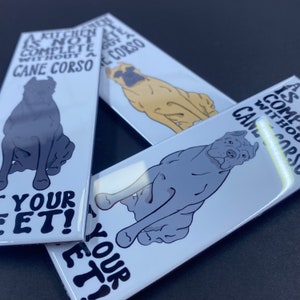May include: Three white rectangular magnets with a black and white illustration of a Cane Corso dog. The text on the magnets reads "A kitchen is not complete without a Cane Corso - Lick your feet!"