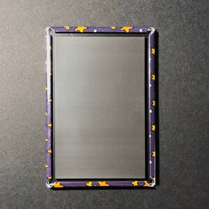 Puede incluir: Un letrero rectangular de metal con fondo negro y borde morado. El borde est&aacute; decorado con un patr&oacute;n repetitivo de estrellas amarillas sobre fondo morado.