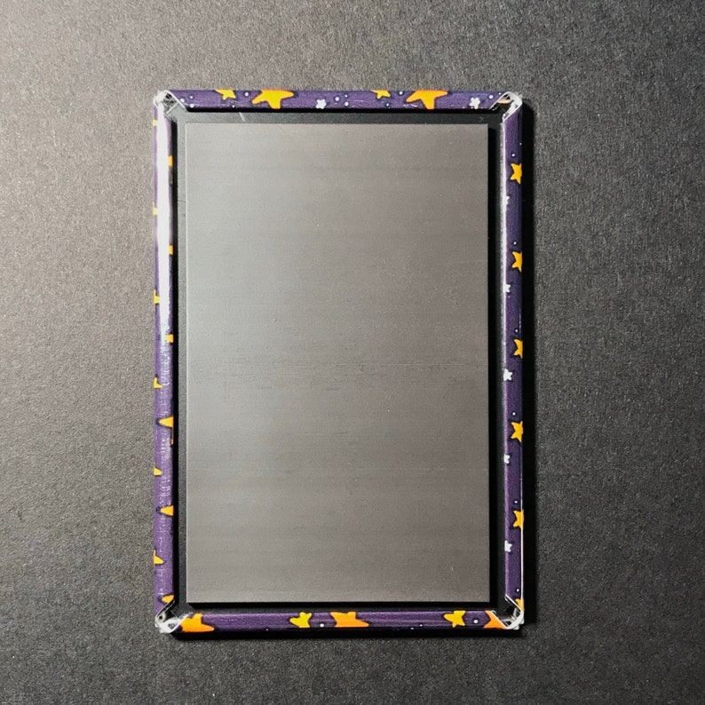 Puede incluir: Un letrero rectangular de metal con fondo negro y borde morado. El borde est&aacute; decorado con un patr&oacute;n repetitivo de estrellas amarillas sobre fondo morado.