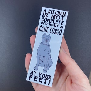 May include: A white rectangular magnet with black text that reads "A kitchen is not complete without a Cane Corso at your feet!" and a black and white illustration of a Cane Corso dog.