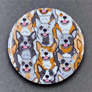 May include: A round coaster with a pattern of cartoon Australian Shepherd dogs. The dogs are all smiling and have different colored markings. The text "The Cloudy Corgi" is in the center of the coaster.