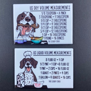May include: Two white rectangular magnets with a cartoon dog illustration. The top magnet has the text "US DRY VOLUME MEASUREMENTS" and lists dry volume conversions. The bottom magnet has the text "US LIQUID VOLUME MEASUREMENTS" and lists liquid volume conversions.