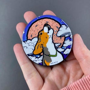 K&ouml;nnte beinhalten: Ein runder, bunter Magnet mit einem Cartoon-Beagle-Hund, der zum Mond heult. Der Mond ist rosa und orange mit wei&szlig;en Wolken, die ihn umgeben. Der Text "The Cloudy Gang" ist am unteren Rand des Magneten sichtbar.