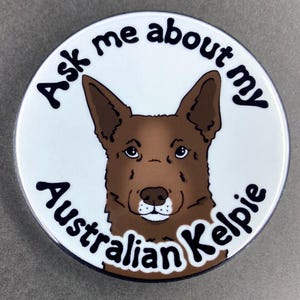 May include: A white round sticker with a brown Australian Kelpie dog illustration. The sticker says "Ask me about my Australian Kelpie" in black text.