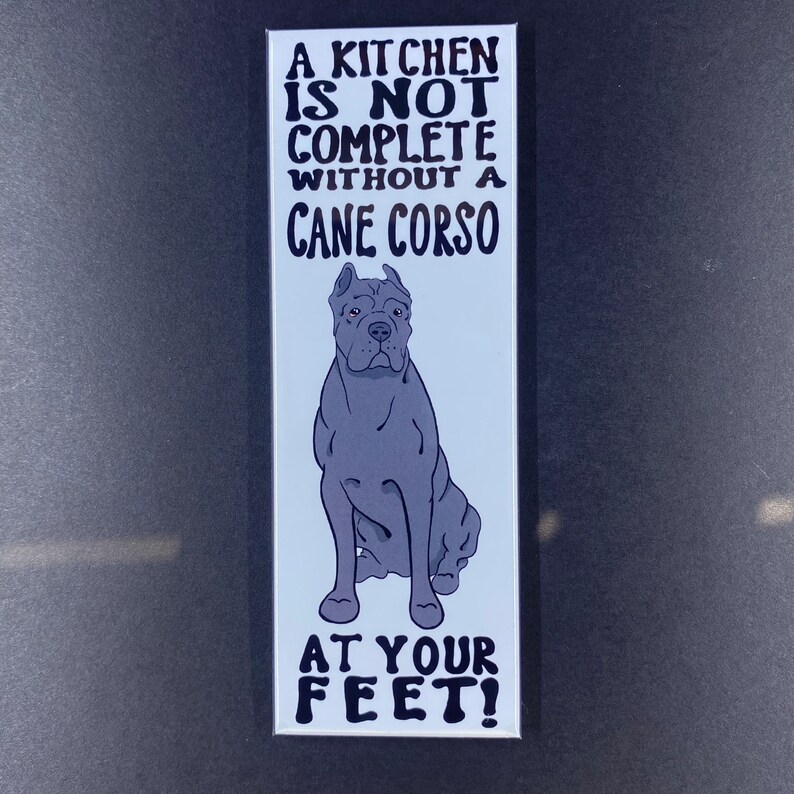 May include: A white rectangular magnet with black text that reads "A kitchen is not complete without a Cane Corso at your feet!" and a black and white illustration of a Cane Corso dog.