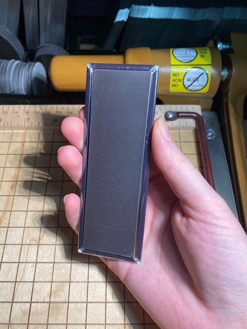 May include: A rectangular black magnet with a silver frame. The magnet is being held in a hand.